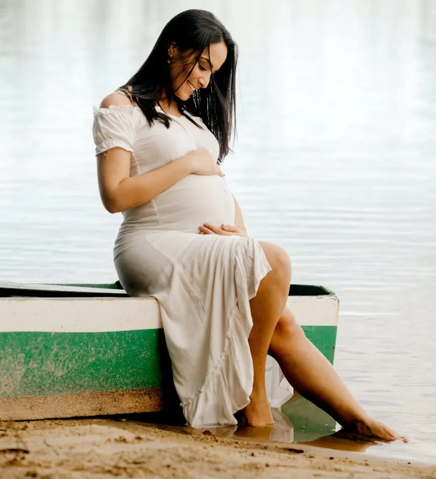 A pregnant woman sitting on the beach by herself.