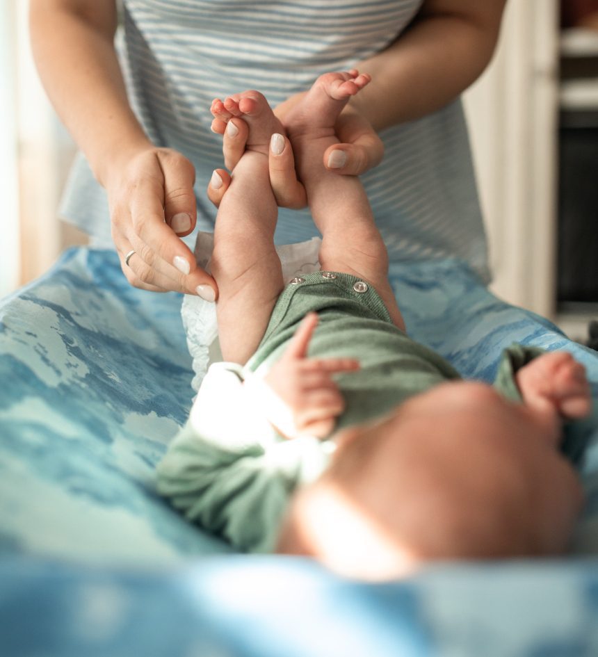 A woman is holding the baby 's feet while they are on the bed.