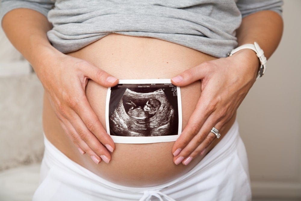 A pregnant woman holding her stomach with an ultrasound image.